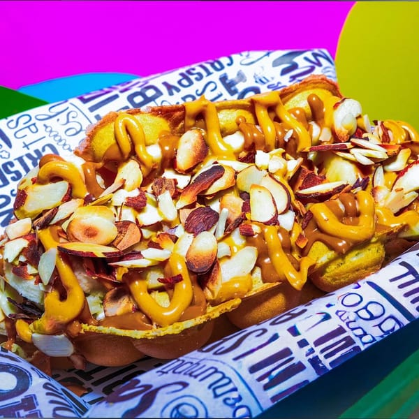 A waffle topped with sliced almonds, banana, and drizzled with peanut butter and caramel sauce.