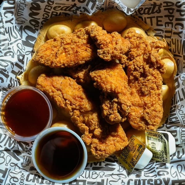 Crispy fried chicken tenders on a bubble waffle with syrup, hot sauce, and butter.