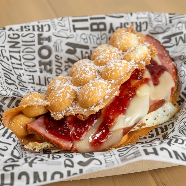 Bubble waffle sandwich with ham, melted cheese, and raspberry jam, dusted with powdered sugar.